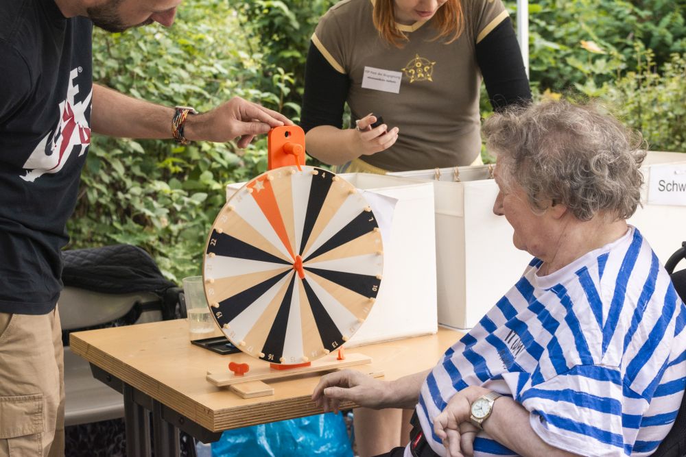 eine Frau mit blau-weiß-geringeltem T-Shirt sitzt im Rollstuhl vor einem Glücksrad