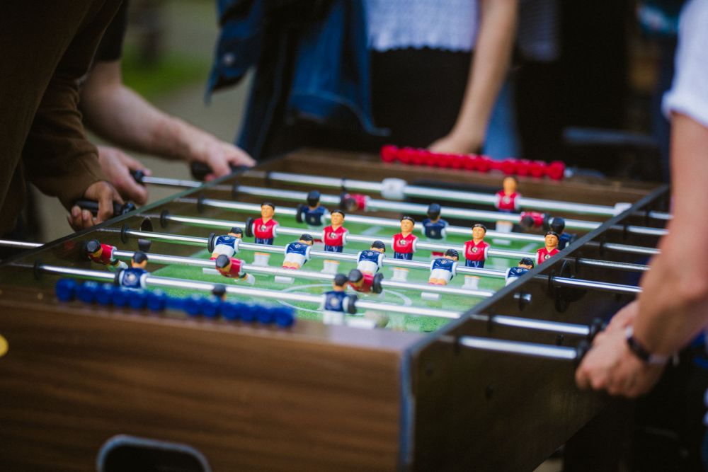 man sieht die Hände von drei Personen, die am Automaten Fußballkicker spielen